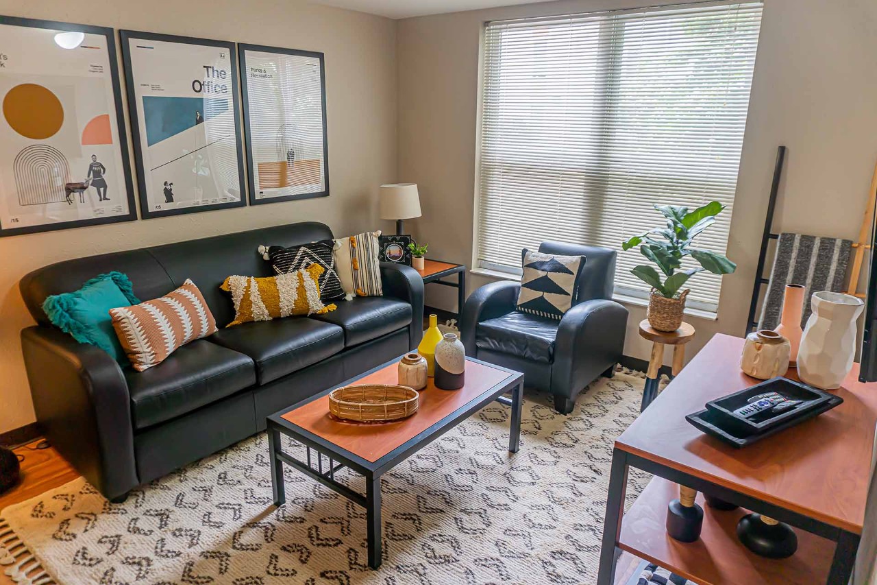 A living room area features a sofa, coffee table, side chair and console. Two windows are at the back.