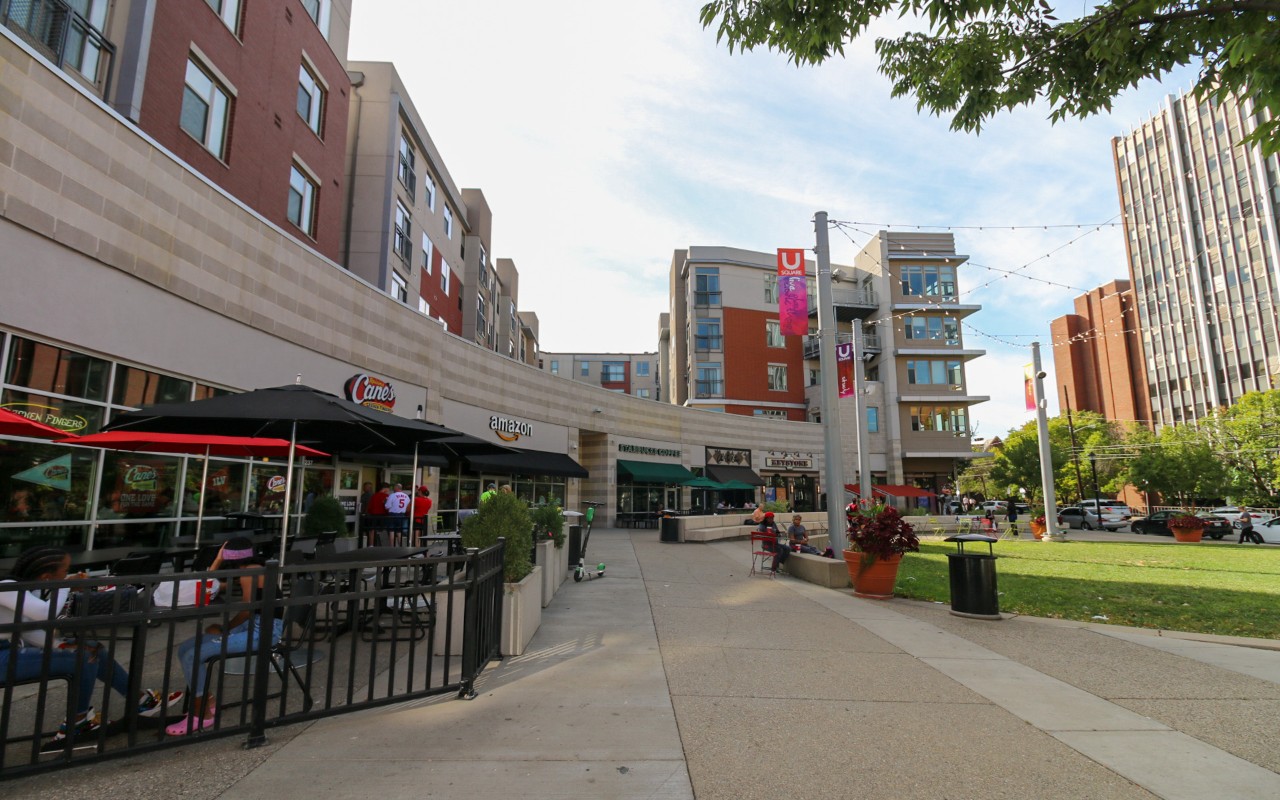 Exterior of the University Square apartments. On the left is an outdoor seating area for a restaurant. There is a grassy open space on the right.
