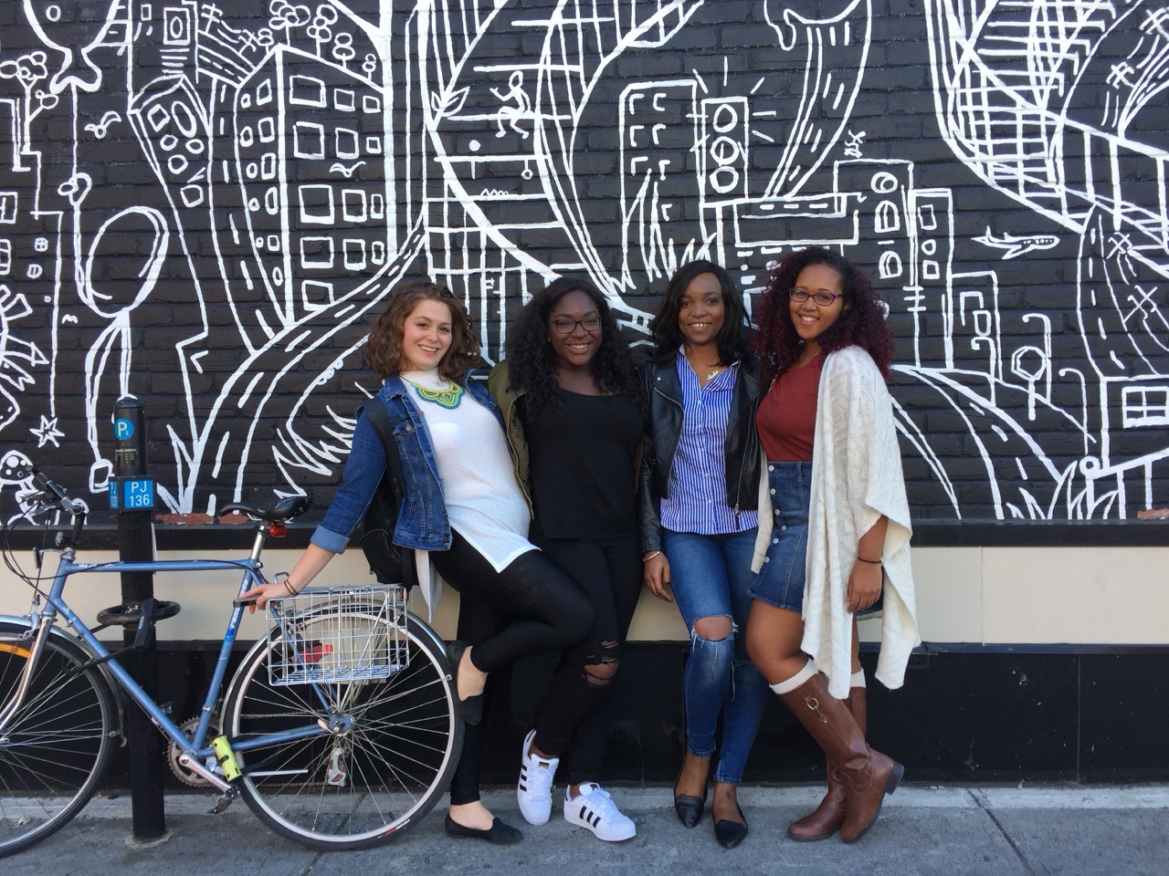 4 students standing in front of a mural 