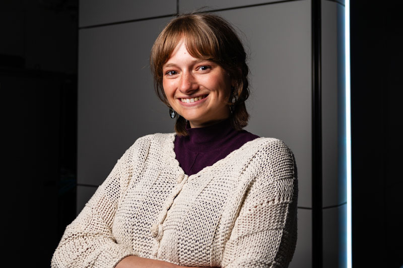 Person smiling at the camera with arms crossed, standing in a modern laboratory setting.