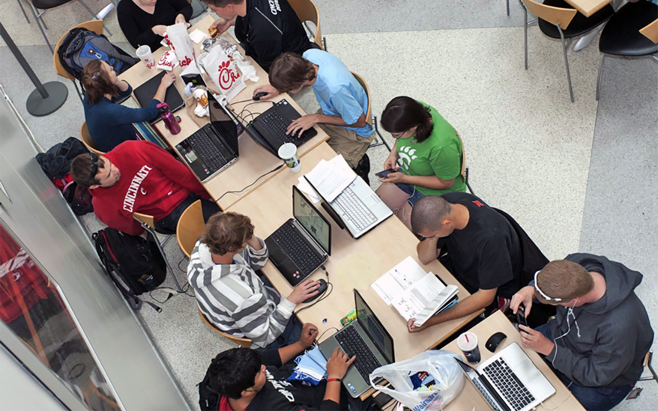 Students gather to eat and study together with their laptops at tables in the food court