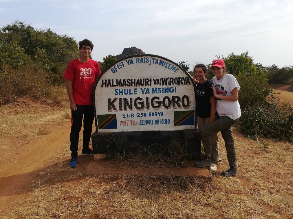 Three students standing by a sign in Tanzania