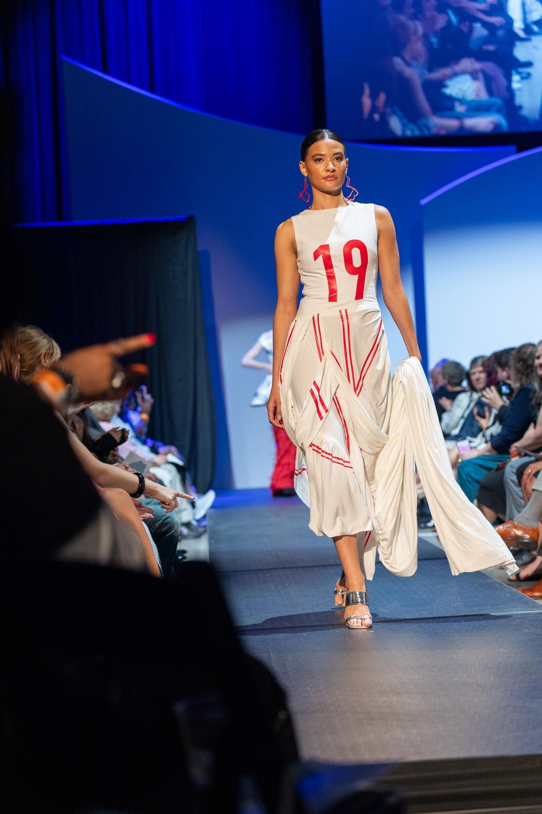 Model wearing a long white dress with the number 19 on the front