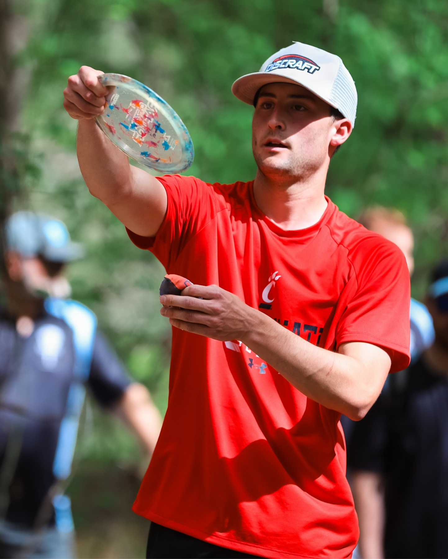 A player in a UC jersey lines up a shot with a disc.