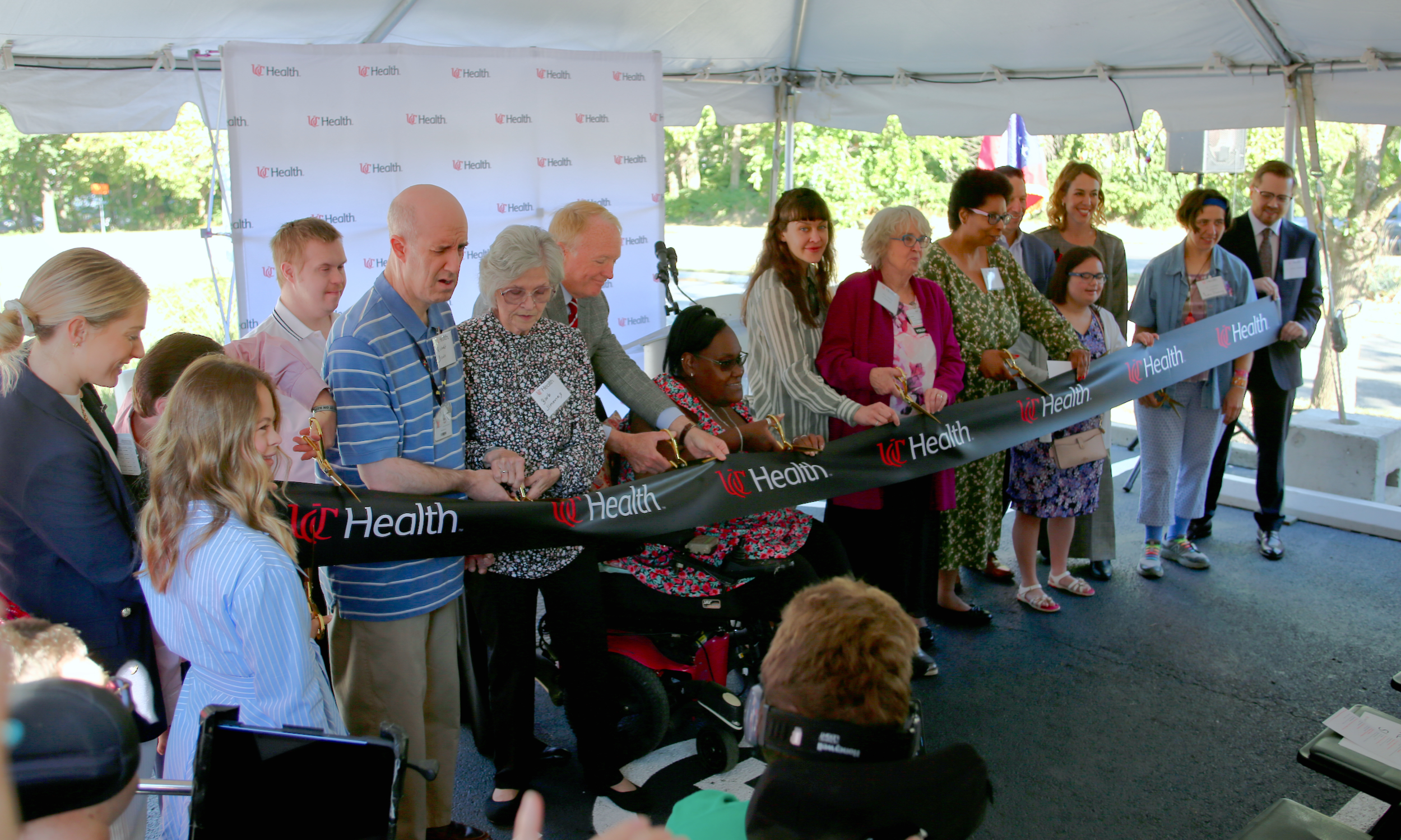 Several people stand in front of a new medical clinic cutting a large red ribbon.