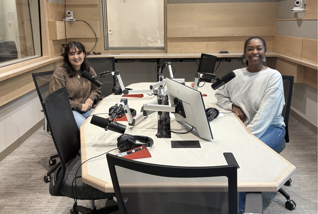 Two people sit at microphones in a radio recording studio.