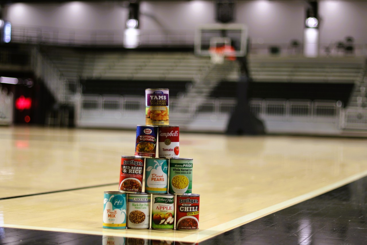 A stack of 10 cans of food on a basketball court.