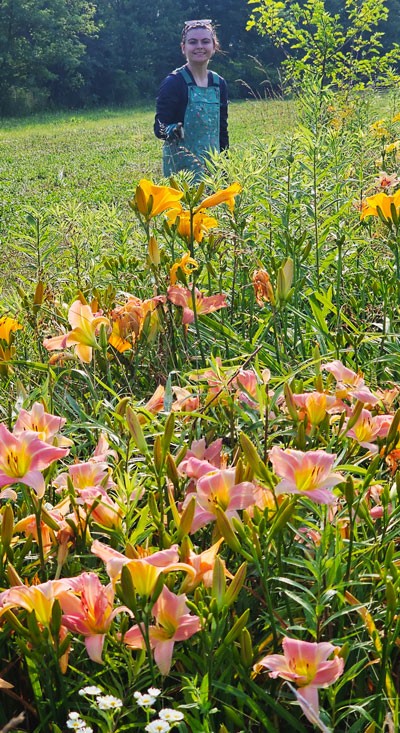 Person standing in a lush field with blooming pink and yellow flowers in the foreground.