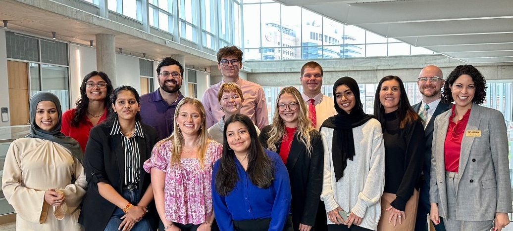 Group of individuals posing together in a well-lit indoor walkway, dressed in professional attire.