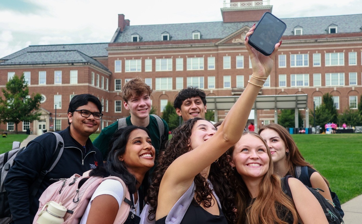 Students in front of the Arts and Sciences building taking a selfie 