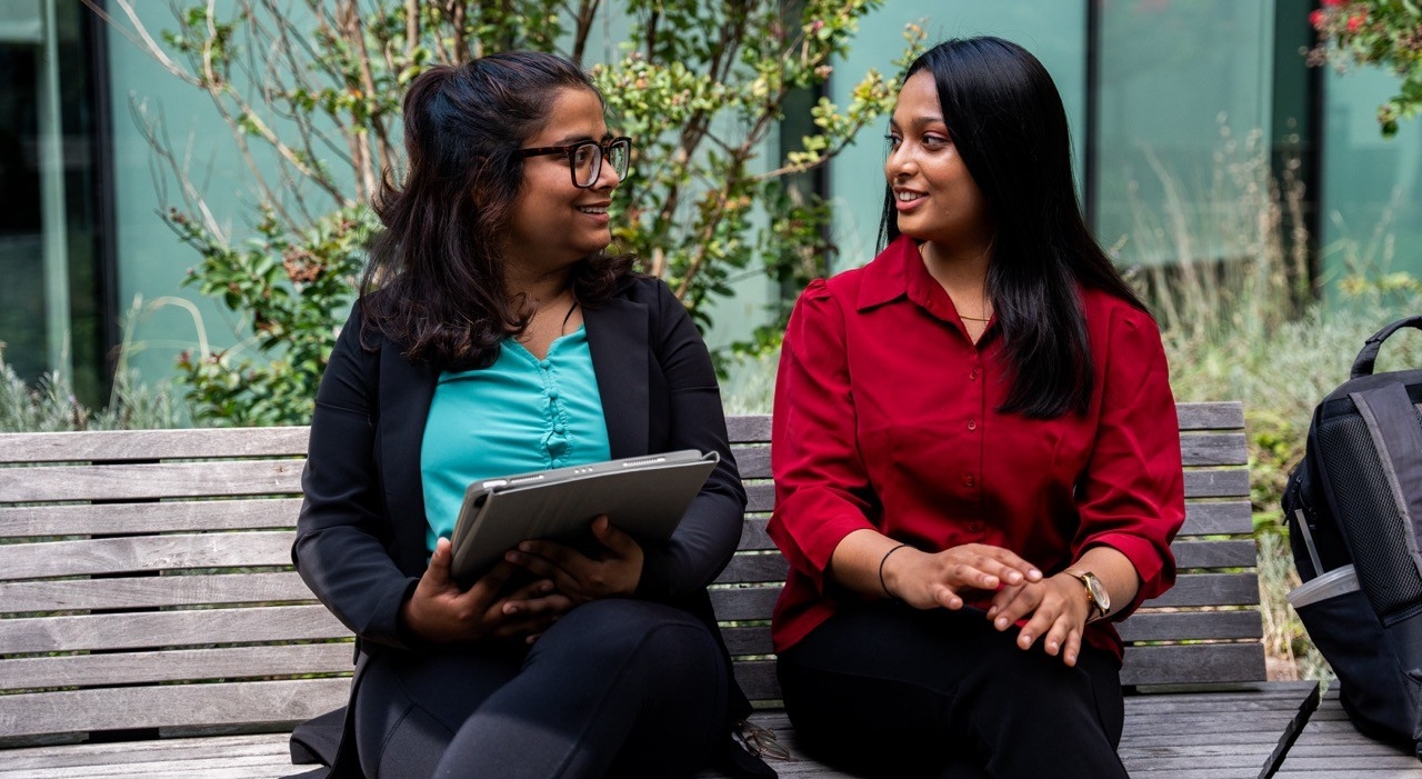 Students sitting on a bench outside talking in professional clothing