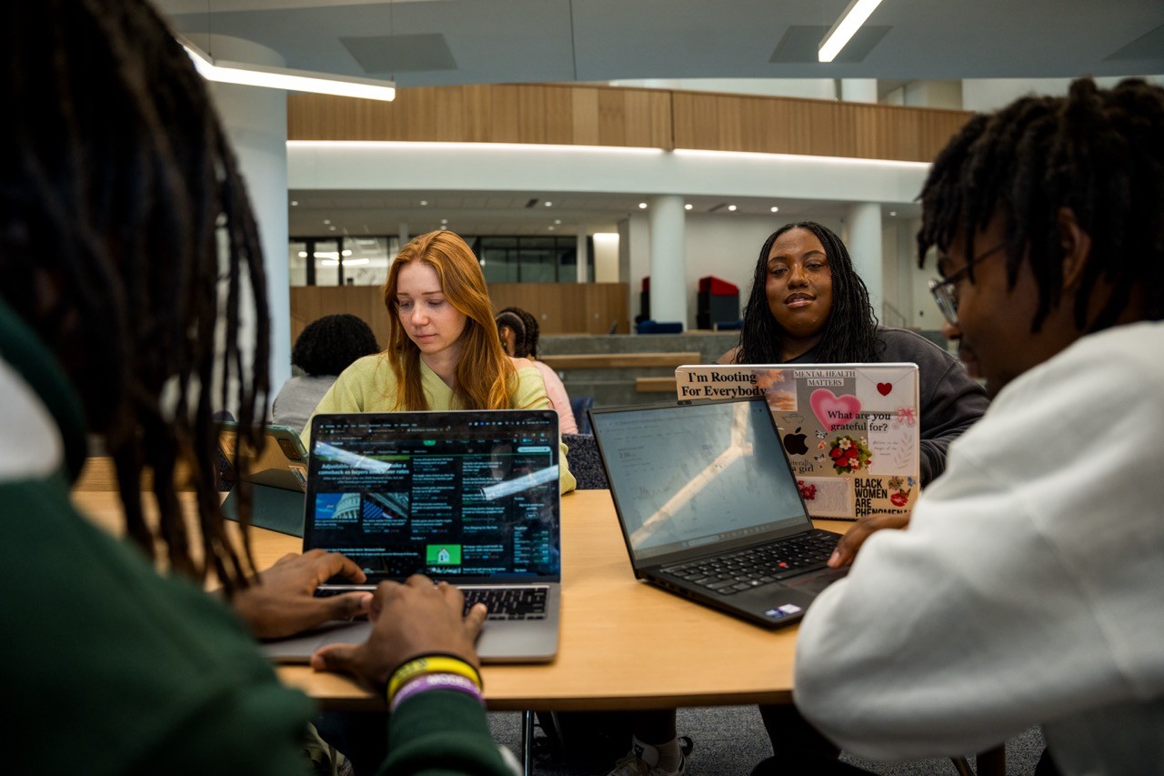 4 students sitting around a table meeting with computers open