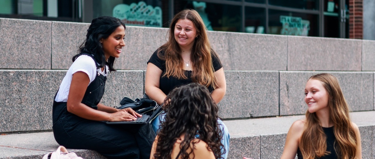 Student sitting in front of Swift hall doing work on computers and talking