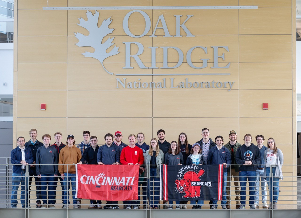 Class standing in front of the Oak Ridge Laboratory sign with a UC Flag 