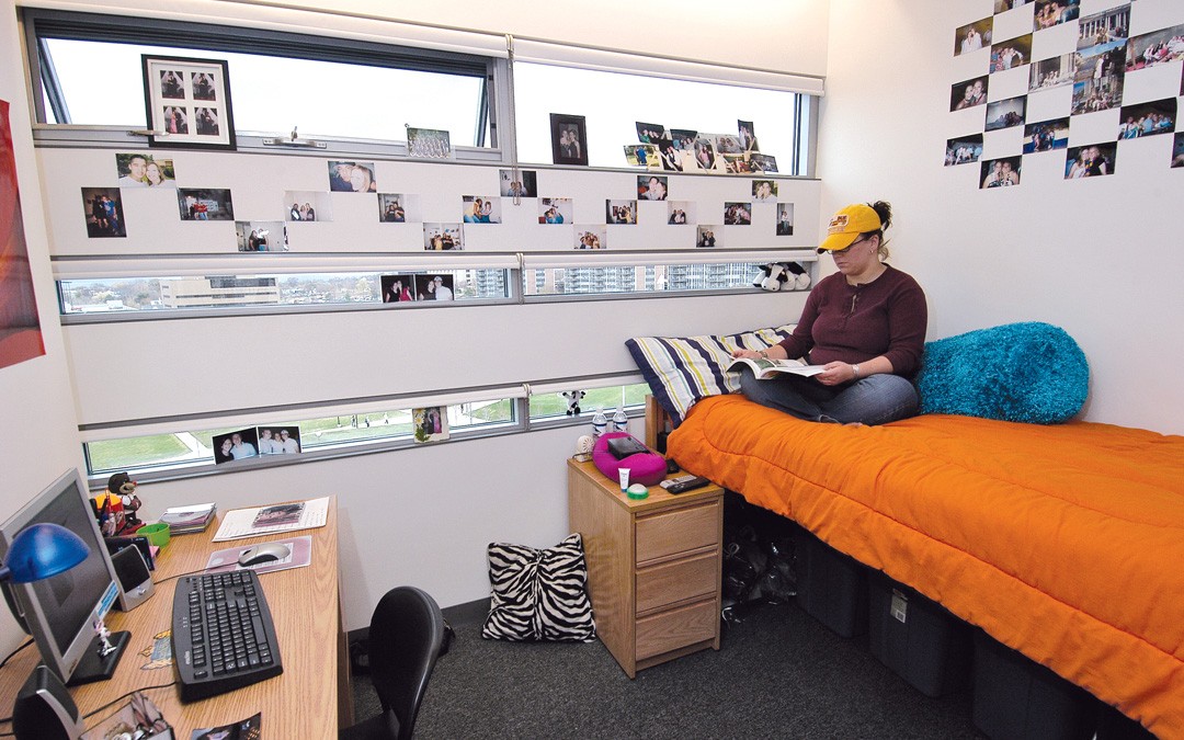 A student is sitting reading on a bed in Campus Recreation Center Hall room.