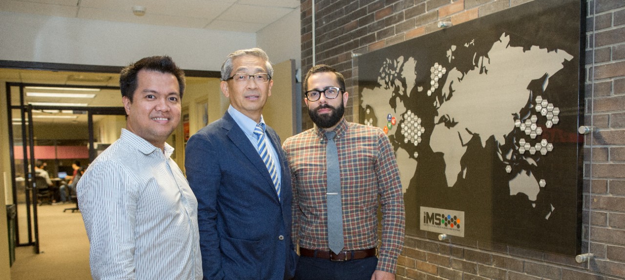Jay Lee poses in front of a world map with Patrick Brown and UC graduate Edzel Lapira