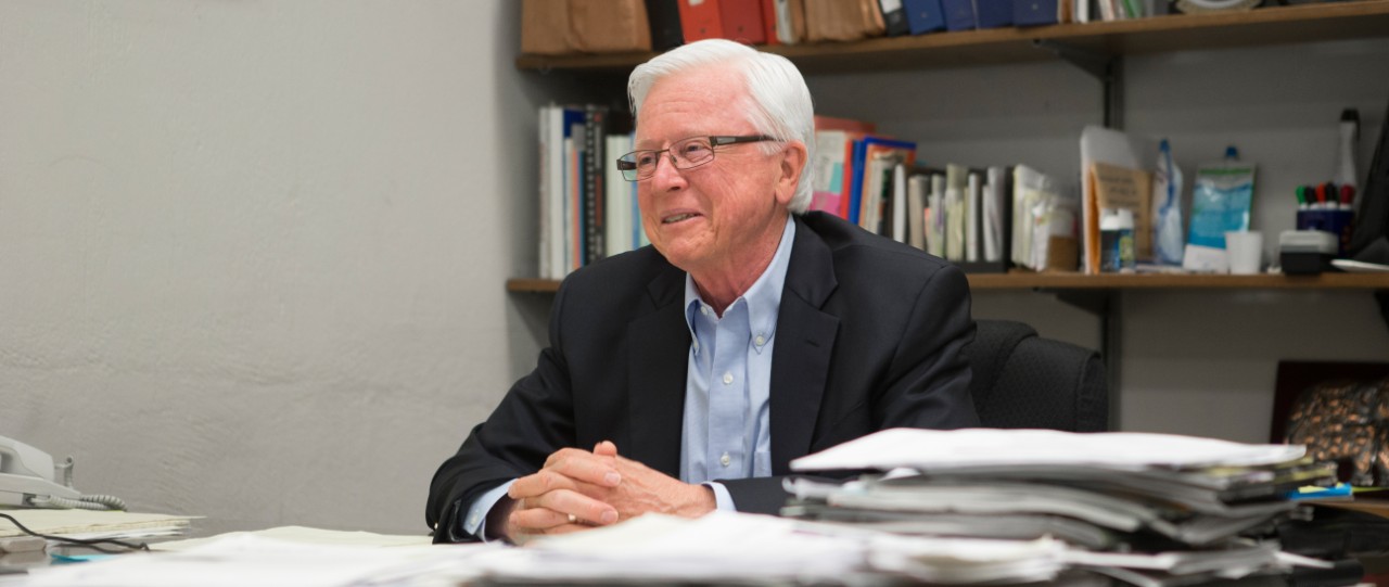William Heineman sits smiling at his desk in his office.