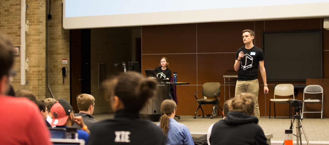 Lewis speaks on stage to auditorium of students