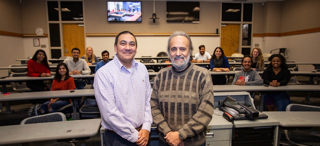 Sustainable Solutions students from UC’s honors program sit in classroom behind UC’s Neil Choudhury (front left) and Constantine Polychroniou (front right).