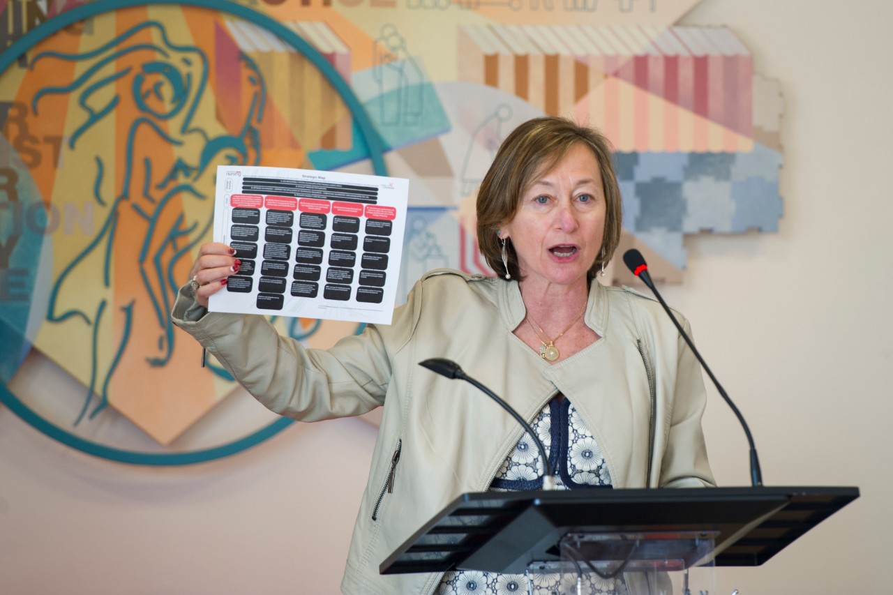 Greer Glazer, dean of the UC College of Nursing speaks at a podium holding a copy of the strategic vision of the college.