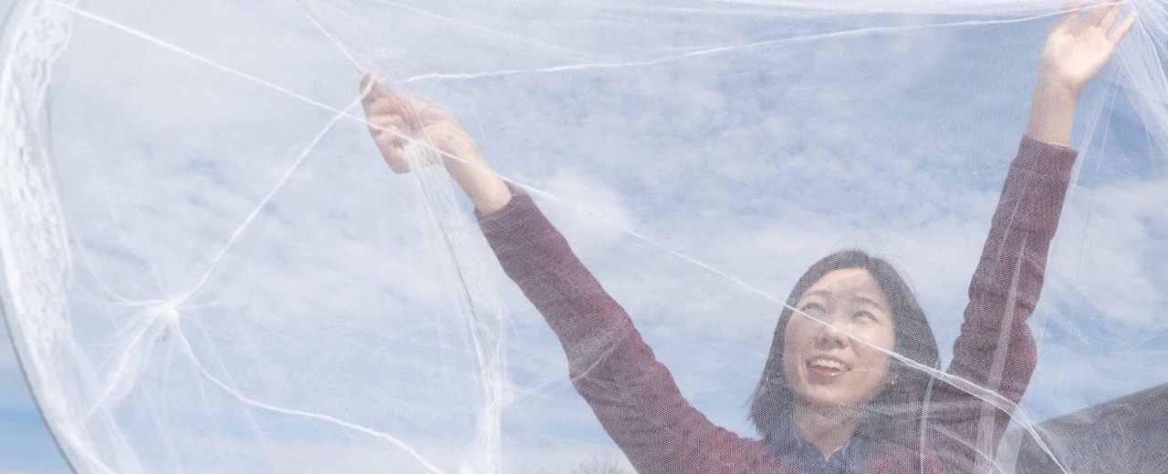 UC student Hana Kim stretches a bed net up to the sky with both hands.