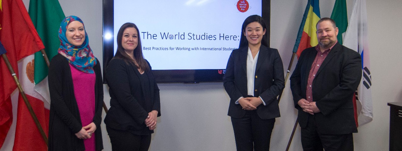 Staff from UC International pose in front of international flags and their logo on a TV screen.