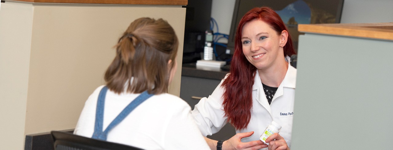 New faculty member Emma Palmer in the skills lab with a student. Palmer explains the side effects of a prescription she is holding in her hands. 
