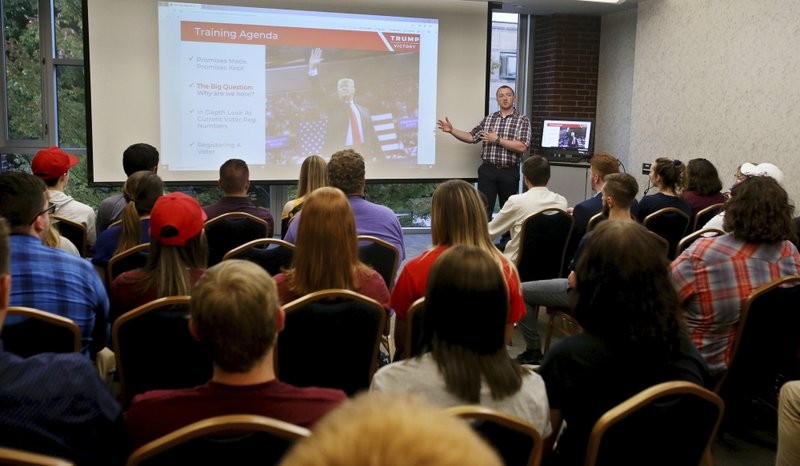 a presenter stands in front of a board in front of a classroom of students