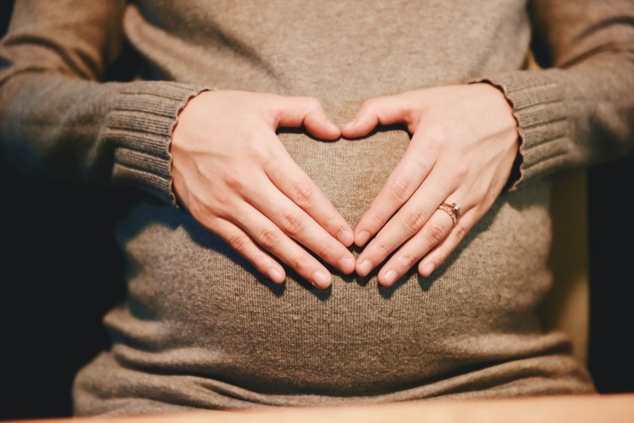 A pregnant woman makes the shape of a heart with her hands on her belly
