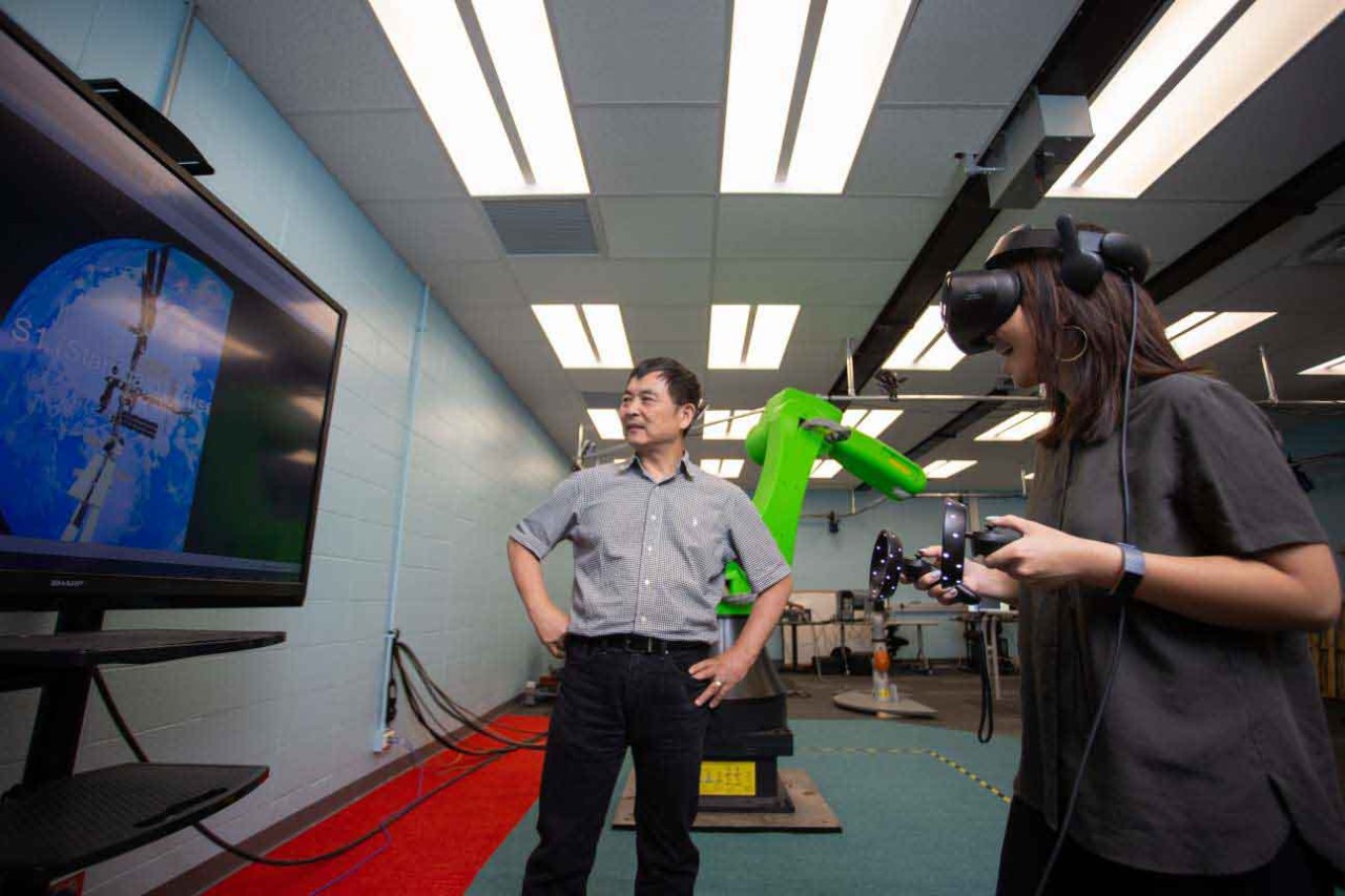 Ou Ma and a student wearing virtual reality goggles work on a project using the International Space Station.