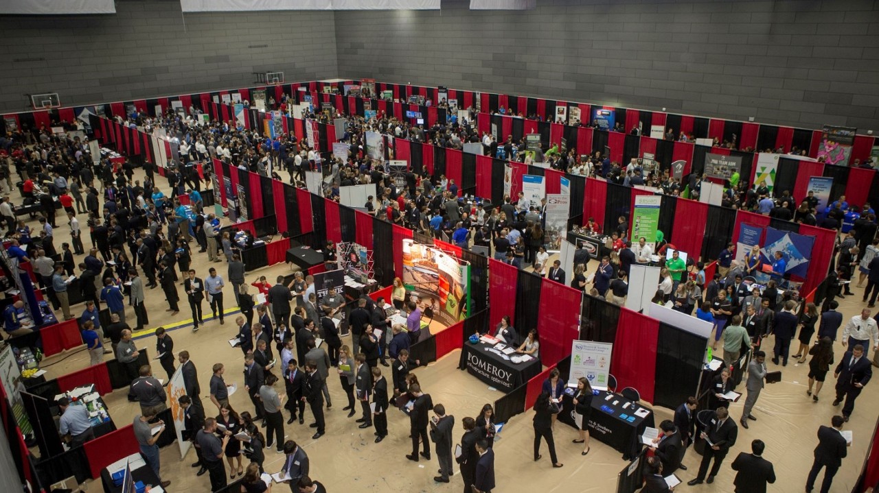 Overhead view of students in suits browsing tables on the floor of the UC Campus Recreation Center