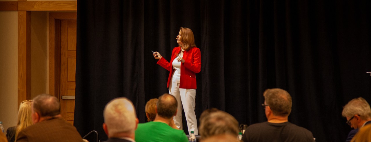 Sonya Hall speaking at event in red business jacket in front of audience.