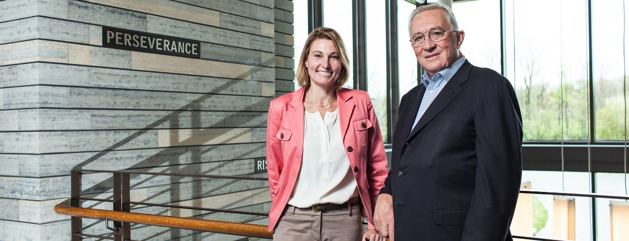 Joni Fedders and Clay Mathile of Aileron, posing on stairway with word "perseverance" behind them on wall.