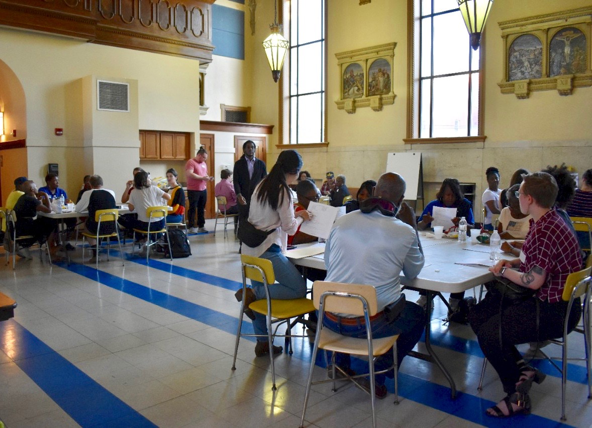 Several UC students sit with residents of South Cumminsville inside a school gym to discuss recycling.