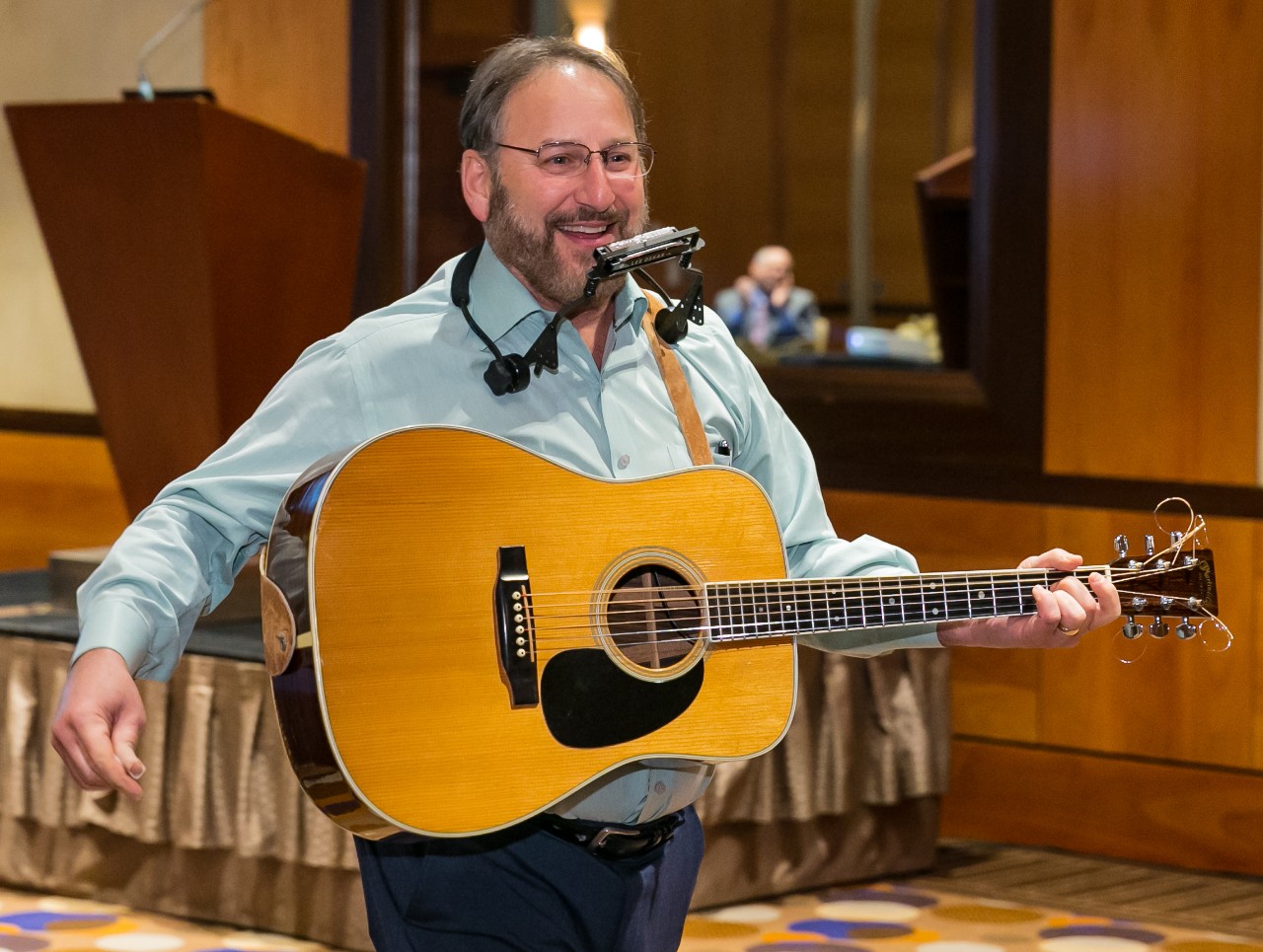a man holding a guitar and wearing a harmonica holder
