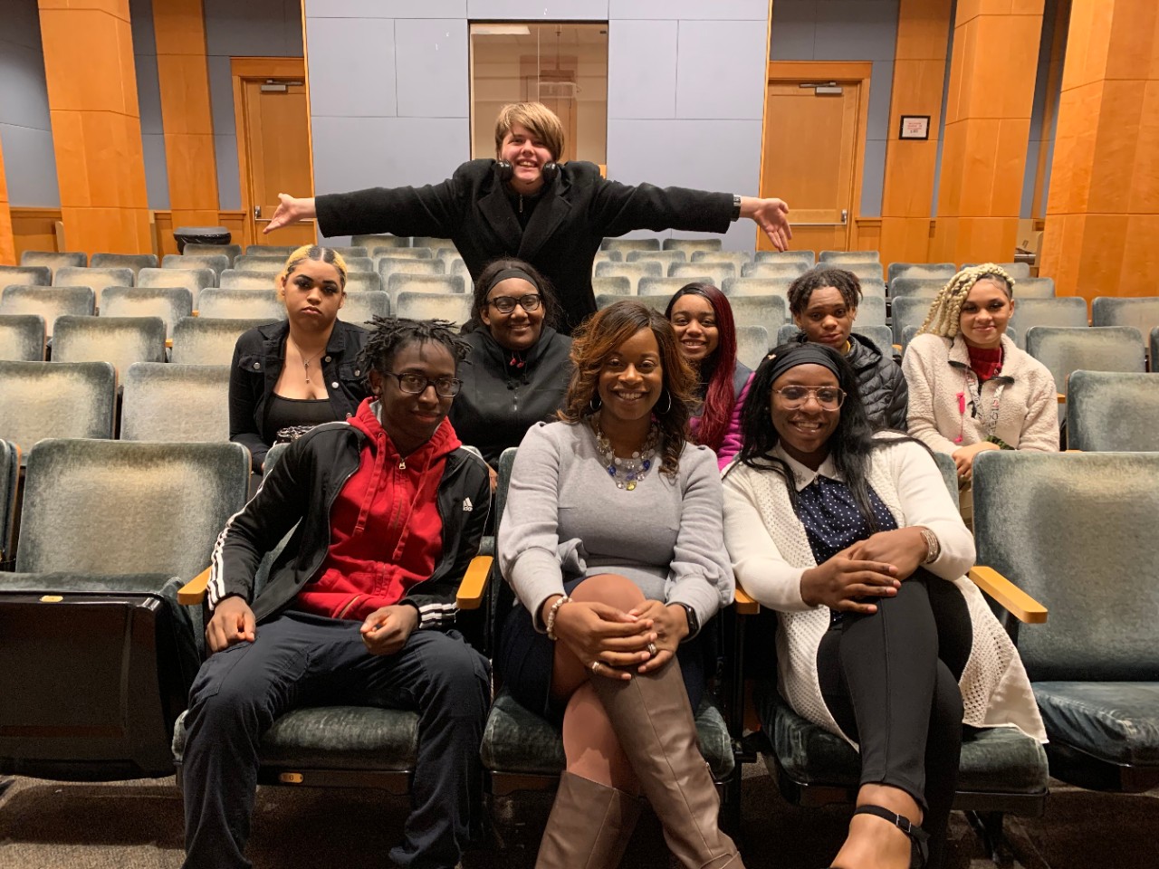 eight high school students sitting around an African-American woman in the center of the group. in a classroom with theatre-style seating