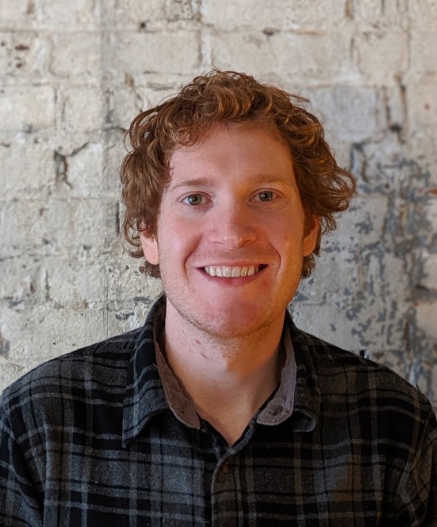 Sean Kennedy smiles for a picture in front of a brick wall.