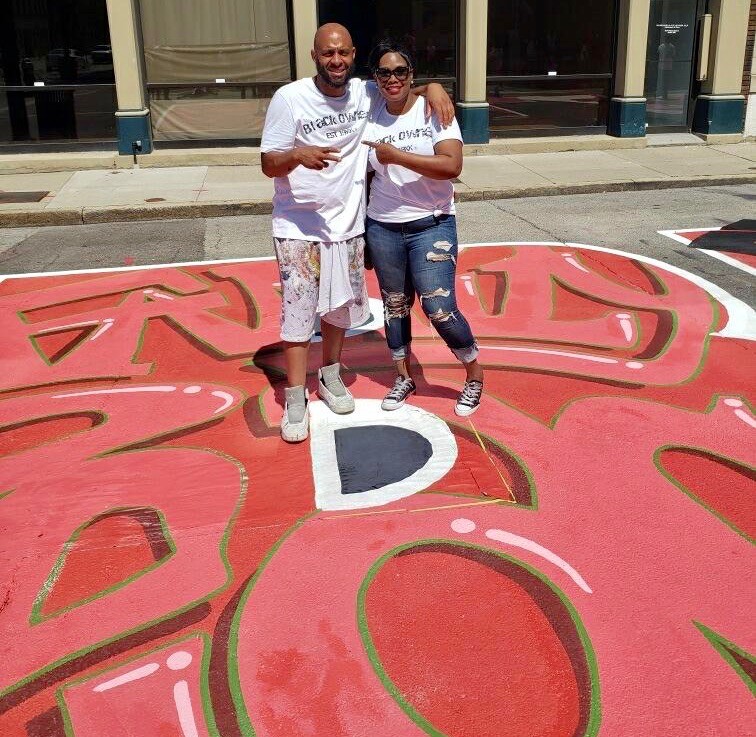 A msn and woman stand together over a red street mural.