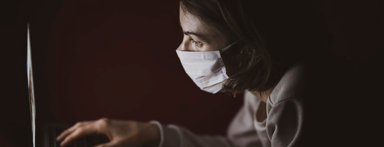 Women wearing a mask typing on a keyboard.