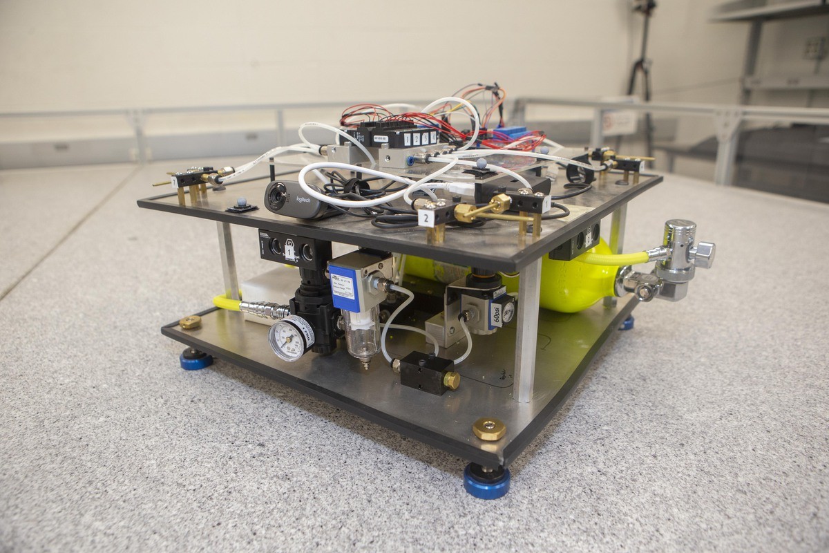 A mock satellite rides a cushion of air on a table surrounded by bumpers.