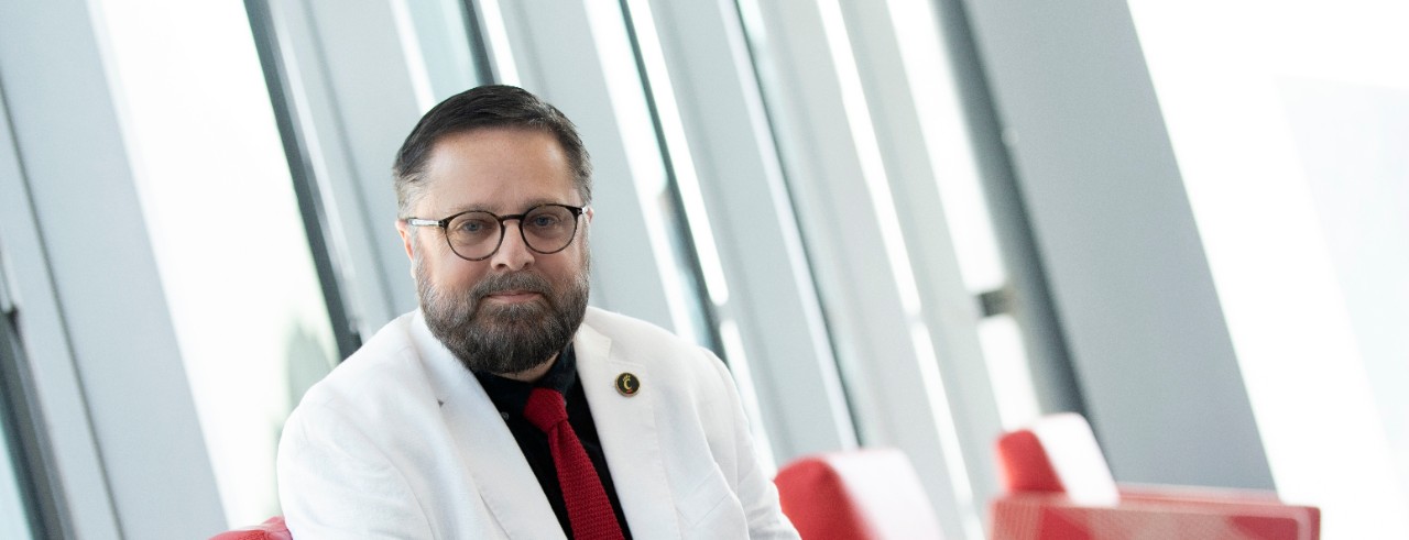 Department of Journalism head Jeffrey Blevins in a white jacket, sitting in a red chair on UC's campus