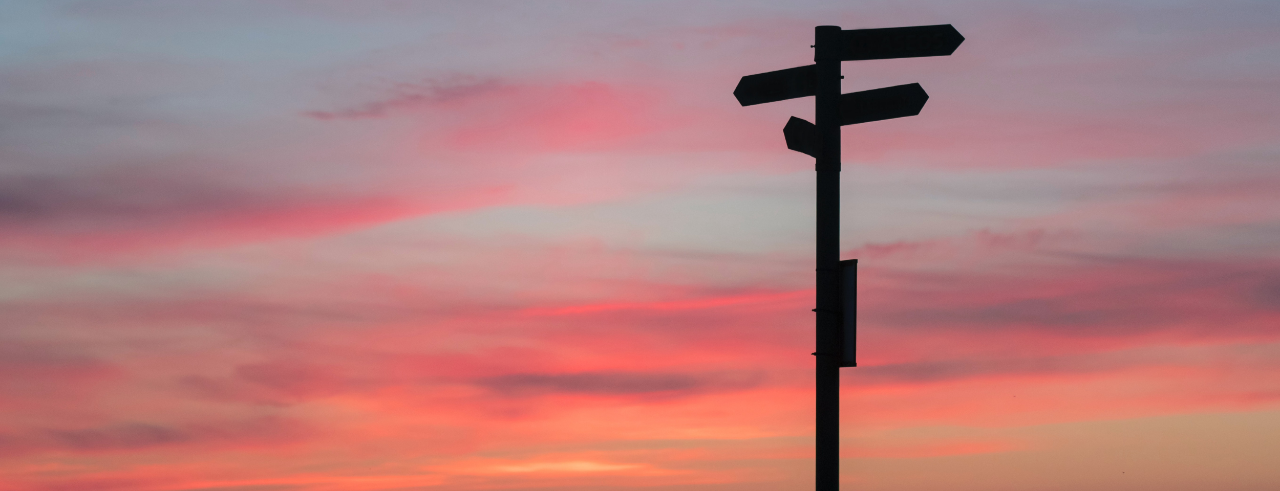 silhouette of a sign post with arrows pointing in multiple directions, with a sunset in the background
