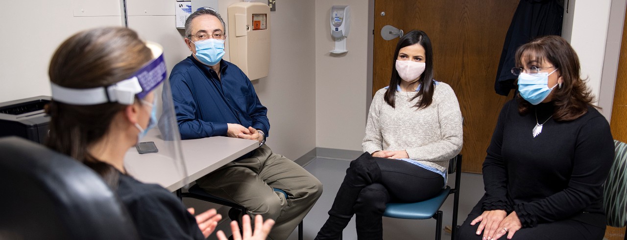 a young woman sitting in a chair between her seated parents listening to a seated doctor whose back is to the camera