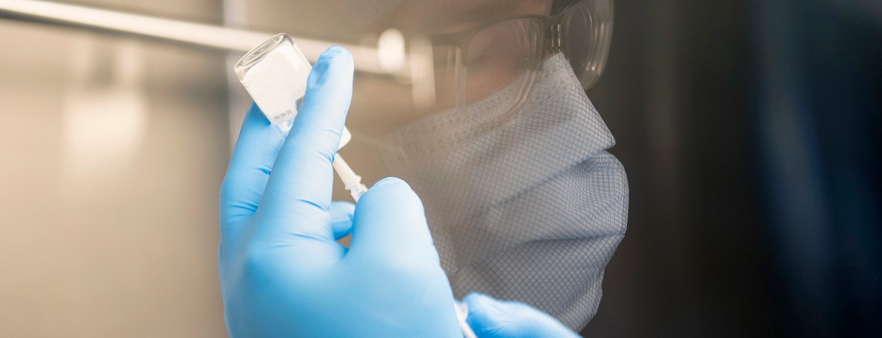 A pharmacist prepares a vaccine dose with their reflection in the laboratory window