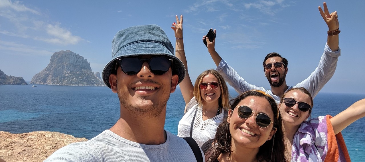 five happy-looking people with arms upraised smile on a sunny beach
