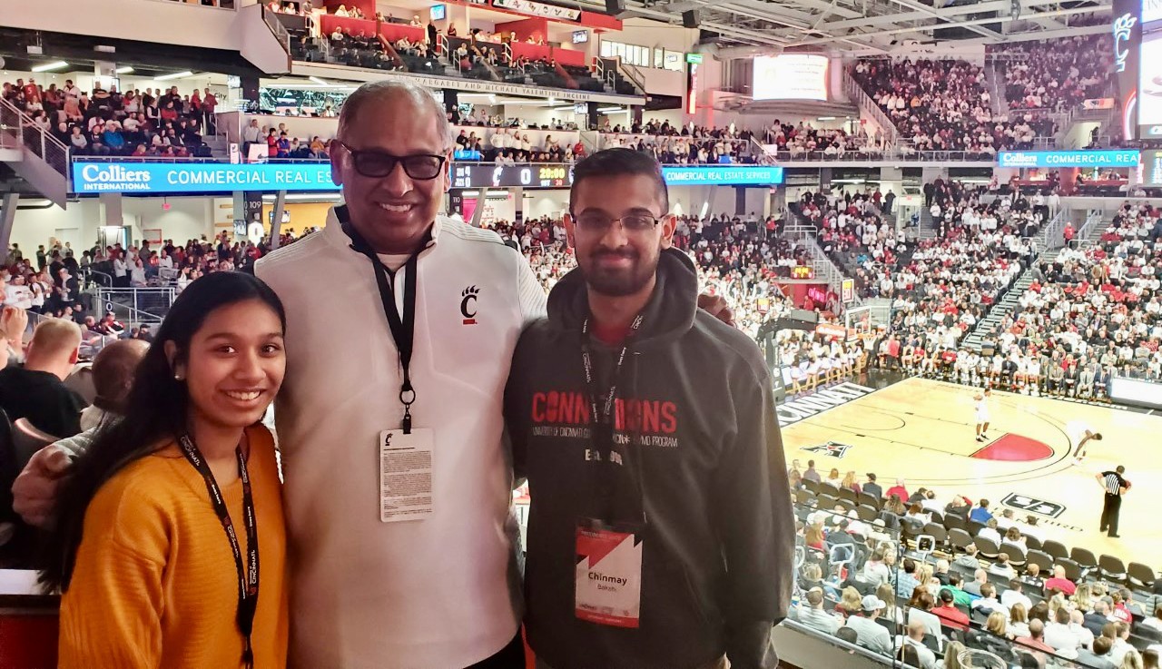 Chinmay Bakshi stands with UC President Neville G. Pinto and a woman in UC's Fifth Third Arena.