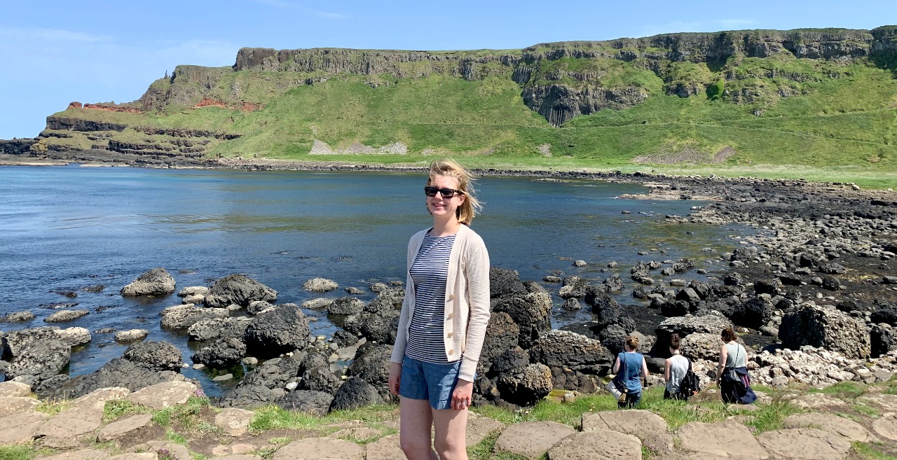 UC's Chloe Elleman stands in front of a rocky ocean shore.