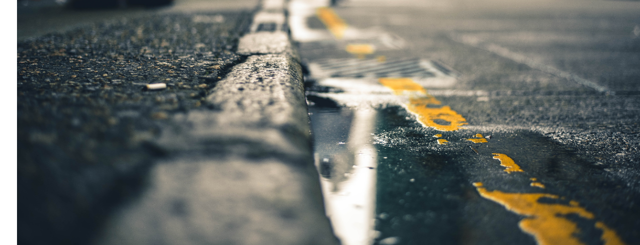 looking down the edge of a curb and a puddle in the gutter
