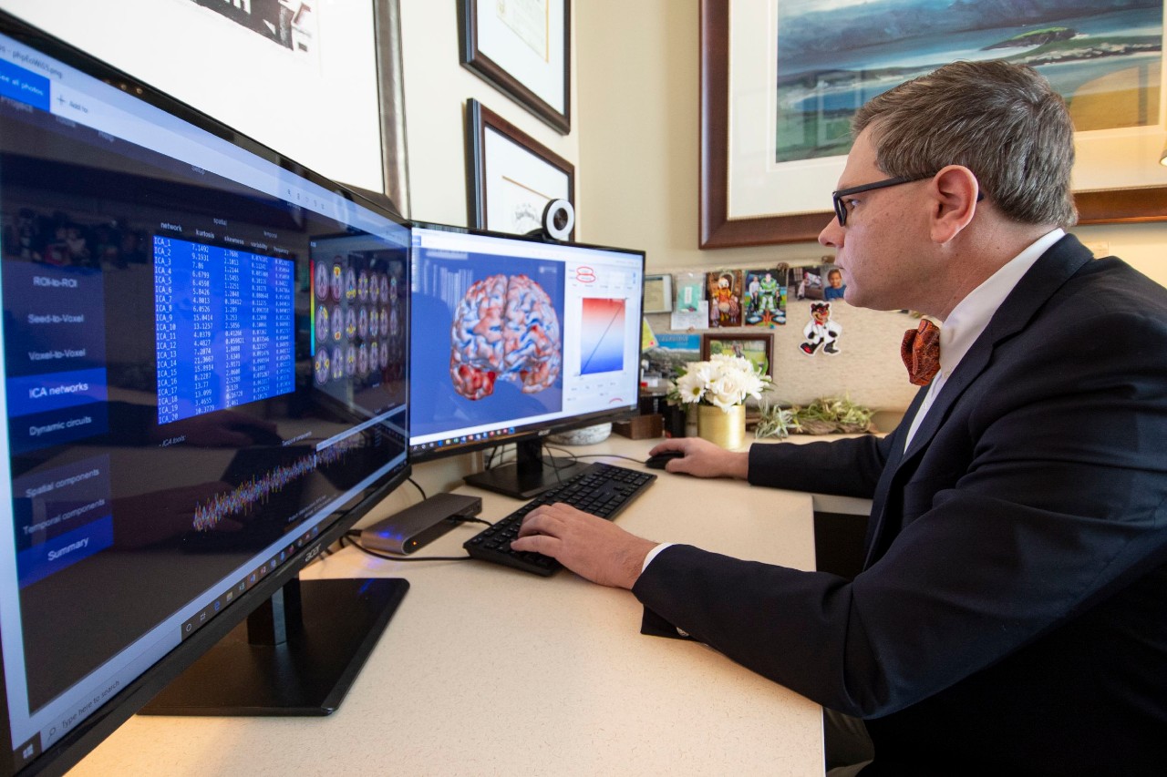 Doctor sits at his desk looking at a picture of a brain and other data on a computer screen