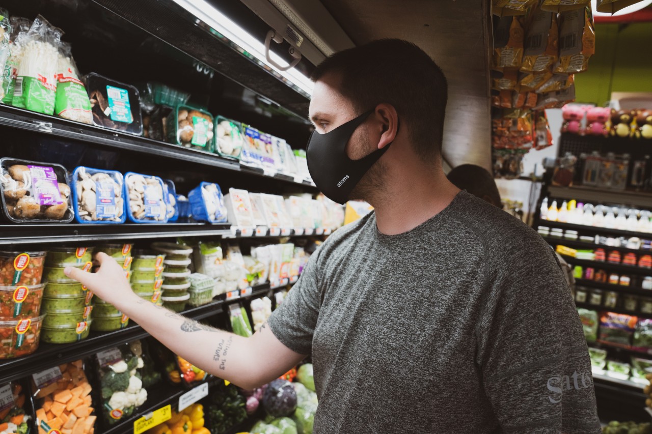 Man wearing a mask picks up an item from a refrigerated grocery store shelf